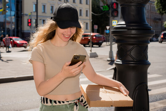 Smiling  Woman Walking While Checking Her Phone and Carrying a Package