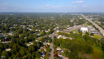 Aerial drone view of Glen Cove, Long Island, showcasing lush green neighborhoods, main roads, and commercial areas under a clear blue sky. A perfect representation of suburban life on Long Island.