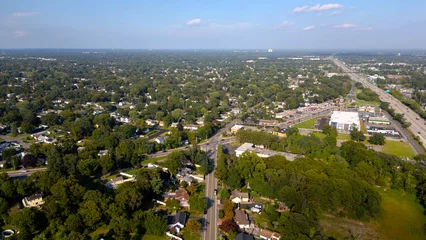 Aerial drone view of Glen Cove, Long Island, showcasing lush green neighborhoods, main roads, and commercial areas under a clear blue sky. A perfect representation of suburban life on Long Island.