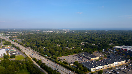 Obraz premium Aerial drone view of Glen Cove, Long Island, showcasing lush green neighborhoods, main roads, and commercial areas under a clear blue sky. A perfect representation of suburban life on Long Island.