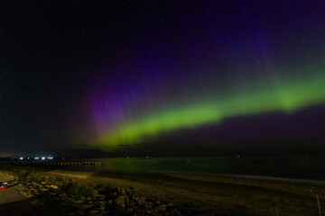 The image is of a beach with houses and a rainbow in the sky. northern lights Lossiemouth Scotland.