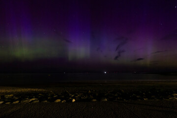 The image is of a beach with houses and a rainbow in the sky. northern lights Lossiemouth Scotland.