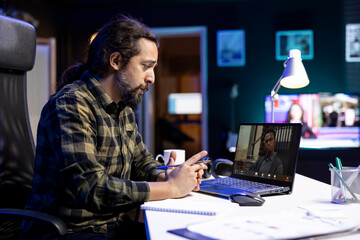 Two multiracial men engaged in a virtual meeting through the laptop. Young bearded man speaking with an individul on a video call, having an online discussion.