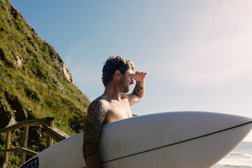 Surfer holding his board while watching the ocean waves on the horizon