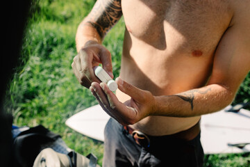 An anonymous shirtless man applying sunscreen to his bo
