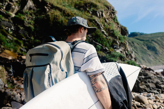 A beginner surfer looking for a surf spot through a rocky beach