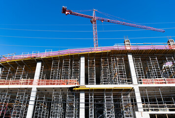 Naklejka premium Building and construction. Hoisting crane. Construction at building site with crane. Construction crane at building area. Construction site with building crane. Industrial area. Site inspection