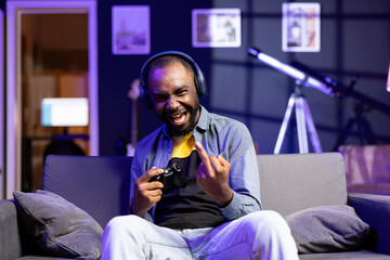 Brass gamer on couch at home insulting rival players while playing competitive multiplayer...