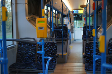 interior of a modern bus, featuring patterned blue seats, yellow ticket validators, and blue handrails