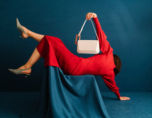 Woman In Red Dress Holding White Handbag Against Blue Background