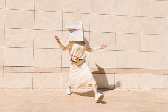 Person With Newspaper Hat Dancing Outdoors Against Wall