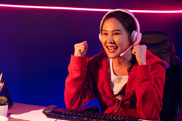 Host channel of smiling beautiful Asian girl streamer playing with raising fist up winning on Esport skilled team players wearing headphones pastel color, fighting online game at neon room. Stratagem.