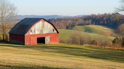 Obraz premium A rustic barn with weathered wood and a classic red paint, set in a rural landscape with rolling hills and open fields.
