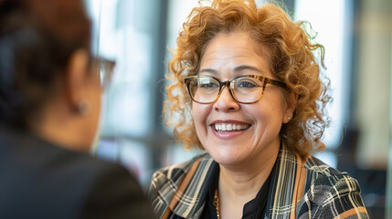 mature Hispanic woman smiles while discussing ideas in corporate office