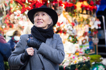 Portrait of smiling elegant aged woman walking along colorful shopping stalls at traditional city...