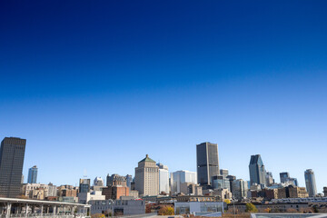 Fototapeta premium Iconic buildings of old Montreal (Vieux Montreal) and CBD business skyscrapers taken from the port under a blue sky, showcasing mix of modern & historic architecture. Montreal is main city of Quebec.