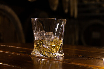 Glass of whisky with ice on old wooden barrel