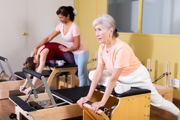Mature European woman practicing Pilates in a group workout with a female instructor trains on a...