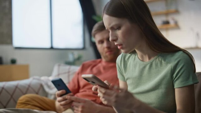 Worried wife showing message smartphone to husband sitting at couch closeup.