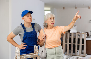 Obraz premium Teenager boy construction assistant talking with senior woman about home improvement works. Aged woman making pointing finger gesture.