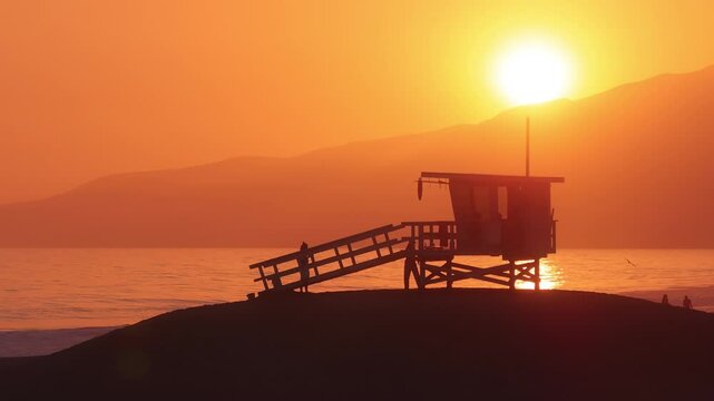 Enjoy the stunning aerial view of a lifeguard tower during sunset in Malibu, California. This serene beach scene features a glowing horizon, creating a picturesque and peaceful atmosphere