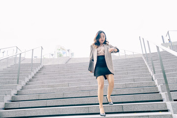 Obraz premium Asian business woman walking to work diligently and briskly in morning in a big city. female in a business suit, dressed in a smart suit, runs to work during rush hour in corridors and stairs.