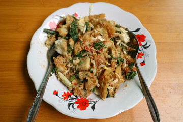 a plate of lotek on wooden table. traditional salad from Indonesia made from mixed vegetables such as spinach, cabbage, tomatoes, bakwan, with peanut sauce and cracker.