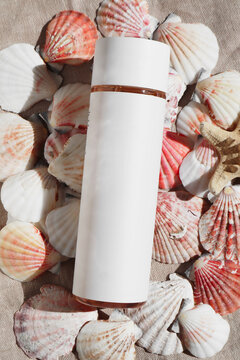 White cosmetic bottle surrounded by seashells 