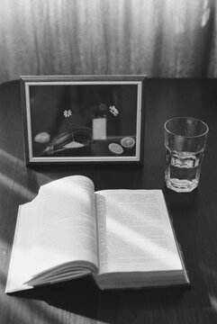 Open book, glass of water and framed picture on the table