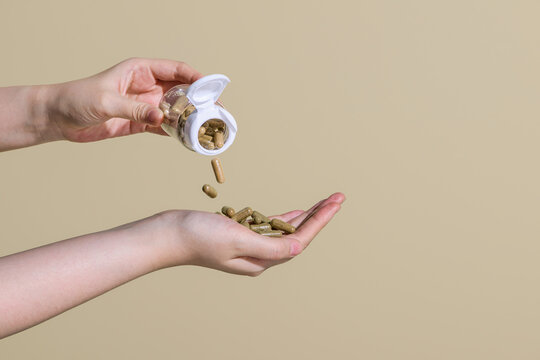 Women's hand pouring herbal pills from a bottle in her hand