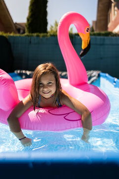 Young girl relaxing on inflatable pink flamingo in swimming pool
