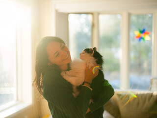 Woman holding cat on hands in the living room of her sunny house