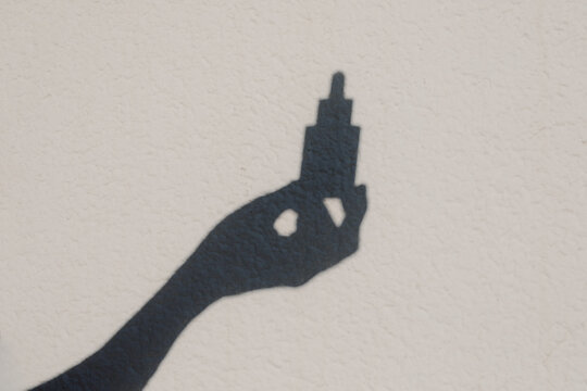 The shadow of an anonymous hand holding a dropper of a beauty product