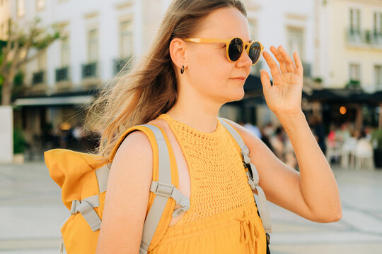 Woman with backpack ajusting sunglasses while walking in the cit