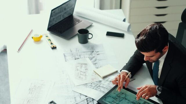 Architect engineer using laptop planning house design at office while sitting at meeting table with blueprint and equipment scatter around.Skilled civil engineer working at blueprint. Alimentation.