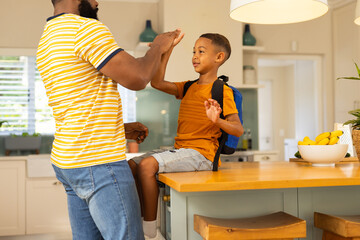High-fiving son with backpack in kitchen, father sending him off to school