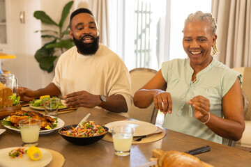Enjoying multigenerational family meal, smiling man and woman sitting at dining table with food