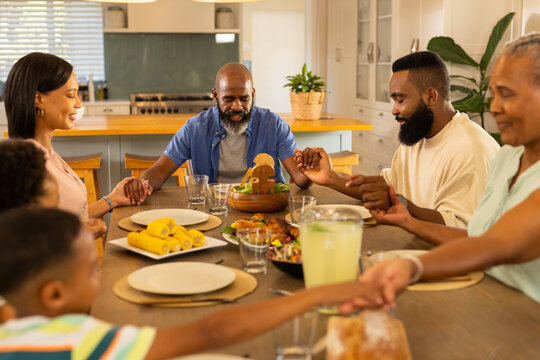 Holding hands, multigenerational family praying before meal at home dining table