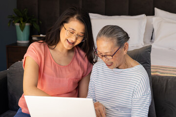 Smiling asian grandmother and granddaughter using laptop together, enjoying quality time at home