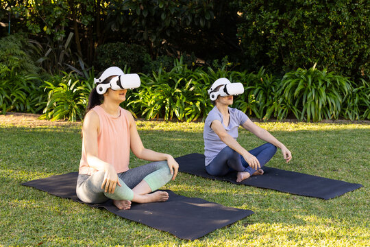 Fototapeta Practicing yoga outdoors, asian grandmother and granddaughter using vr headsets on mats in garden