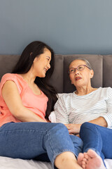 Smiling asian grandmother and granddaughter while sitting on bed, enjoying conversation