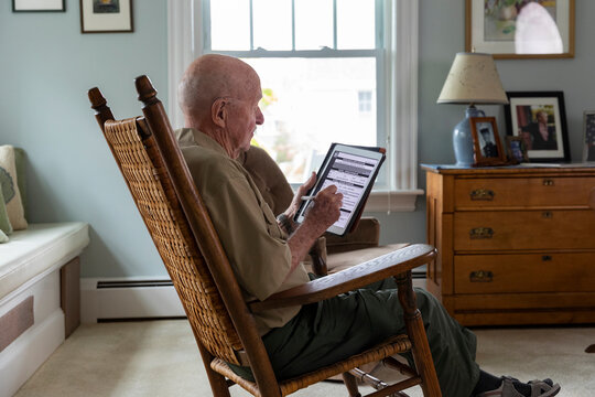 Senior on tablet computer apply Veteran Medical benefits rocking chair - Powered by Adobe