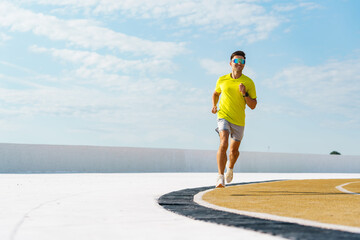 Runner in a bright yellow shirt on a curved track under a vibrant blue sky, exuding energy and focus.