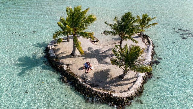 A man and woman alone together on a tiny tropical island in the shape of a heart. The romantic getaway is a private vacation for the married couple in paradise. 