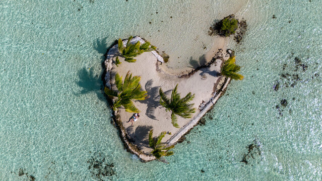 A man and woman alone together on a tiny tropical island in the shape of a heart. The romantic getaway is a private vacation for the married couple in paradise. 