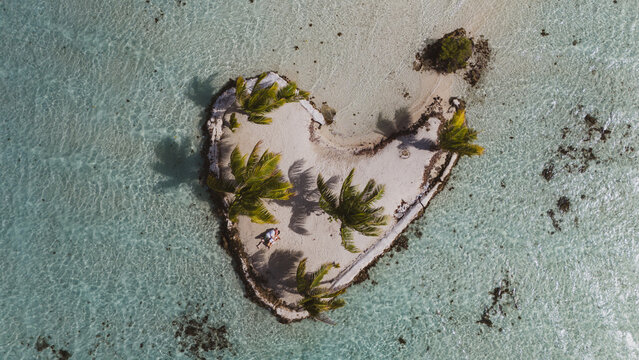 A man and woman alone together on a tiny tropical island in the shape of a heart. The romantic getaway is a private vacation for the married couple in paradise. 