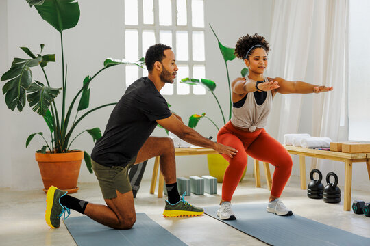 Personal trainer helping a woman doing squats at the gym