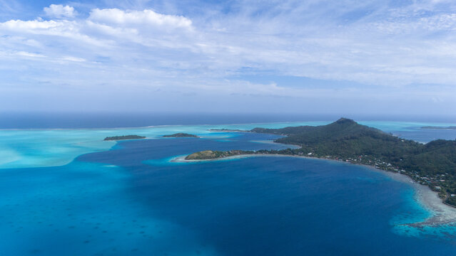 Aerial view captured by drone of the beautiful blue and azure colored ocean sea water surrounding the tropical island of Bora Bora in French Polynesia. 