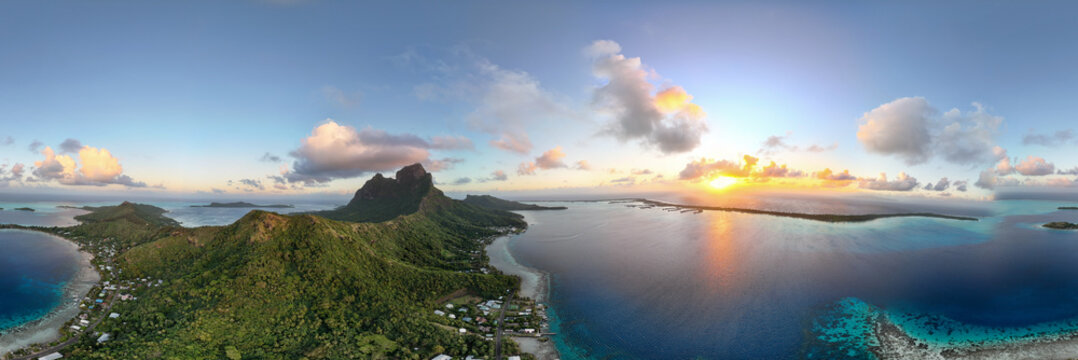 Panoramic view of Bora Bora island surrounded by vibrant azure blue ocean sea in French Polynesia. The water reveals healthy coral reefs under a beautiful sunrise on a pretty morning. 