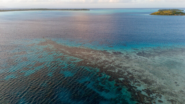Aerial view of vibrant clear azure ocean water. The turquoise blue sea reveals a healthy coral reef known as the point on tropical island Bora Bora.